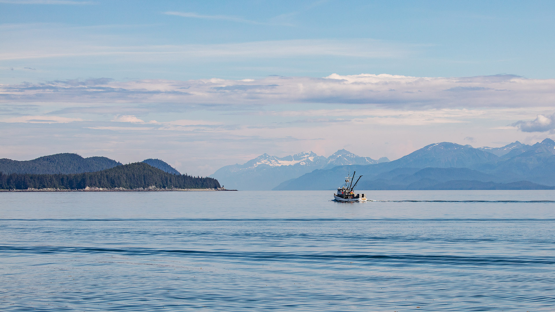 Boat in the middle of the sea Fishing boat on still water with snow-capped mountains behind