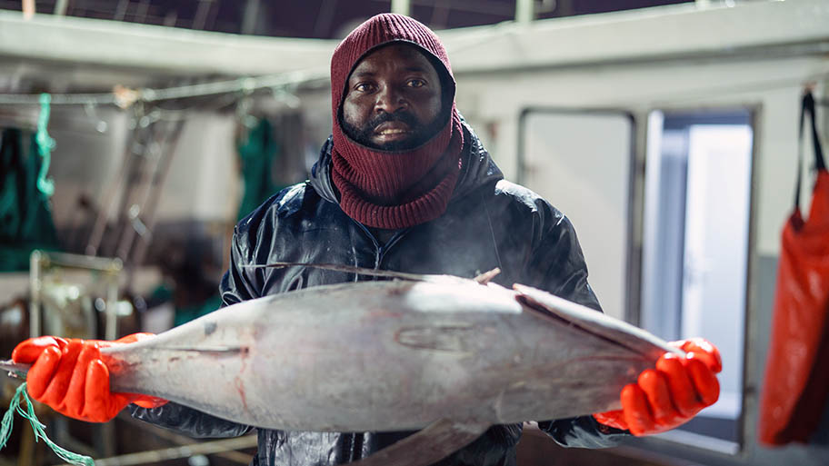 Man in balaclava and gloves holding frozen tuna on boat deck