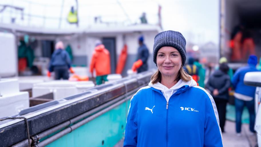 Woman in wooly hat on deck of boat with fishers working behind