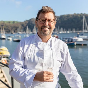 Head and torso shot of man in and white apron holding wine glass: Portrait of chef Mitch Tonks